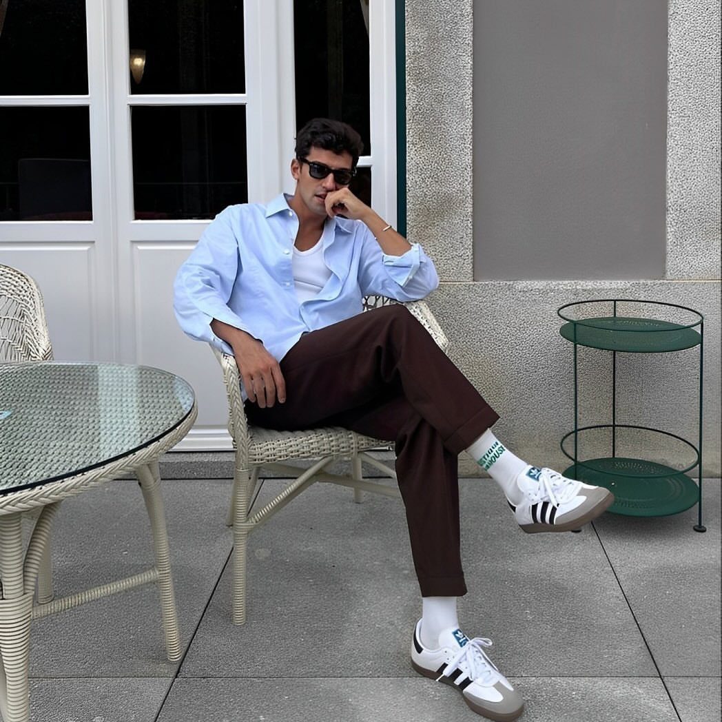 Man in light blue shirt and brown trousers wearing white Adidas Samba sneakers.