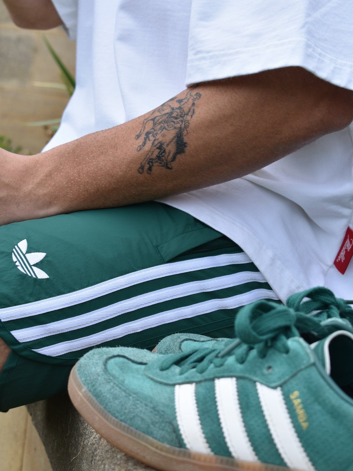 Person wearing green Adidas Samba sneakers, matching green track pants, and a white t-shirt.
