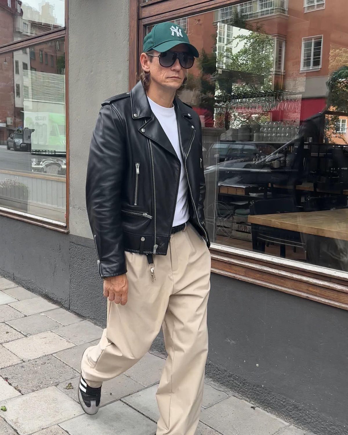 Person wearing a black leather jacket, beige trousers, and black samba sneakers.