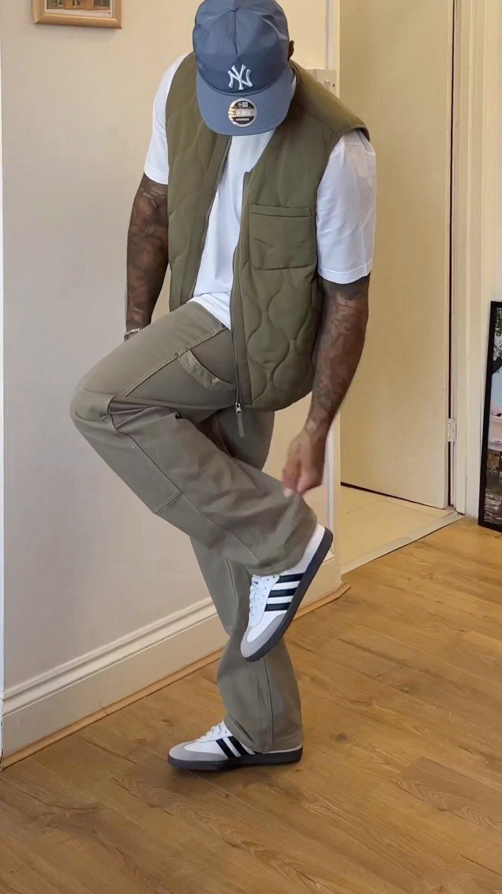 Person wearing olive green cargo pants, quilted vest, and white Adidas Samba sneakers.