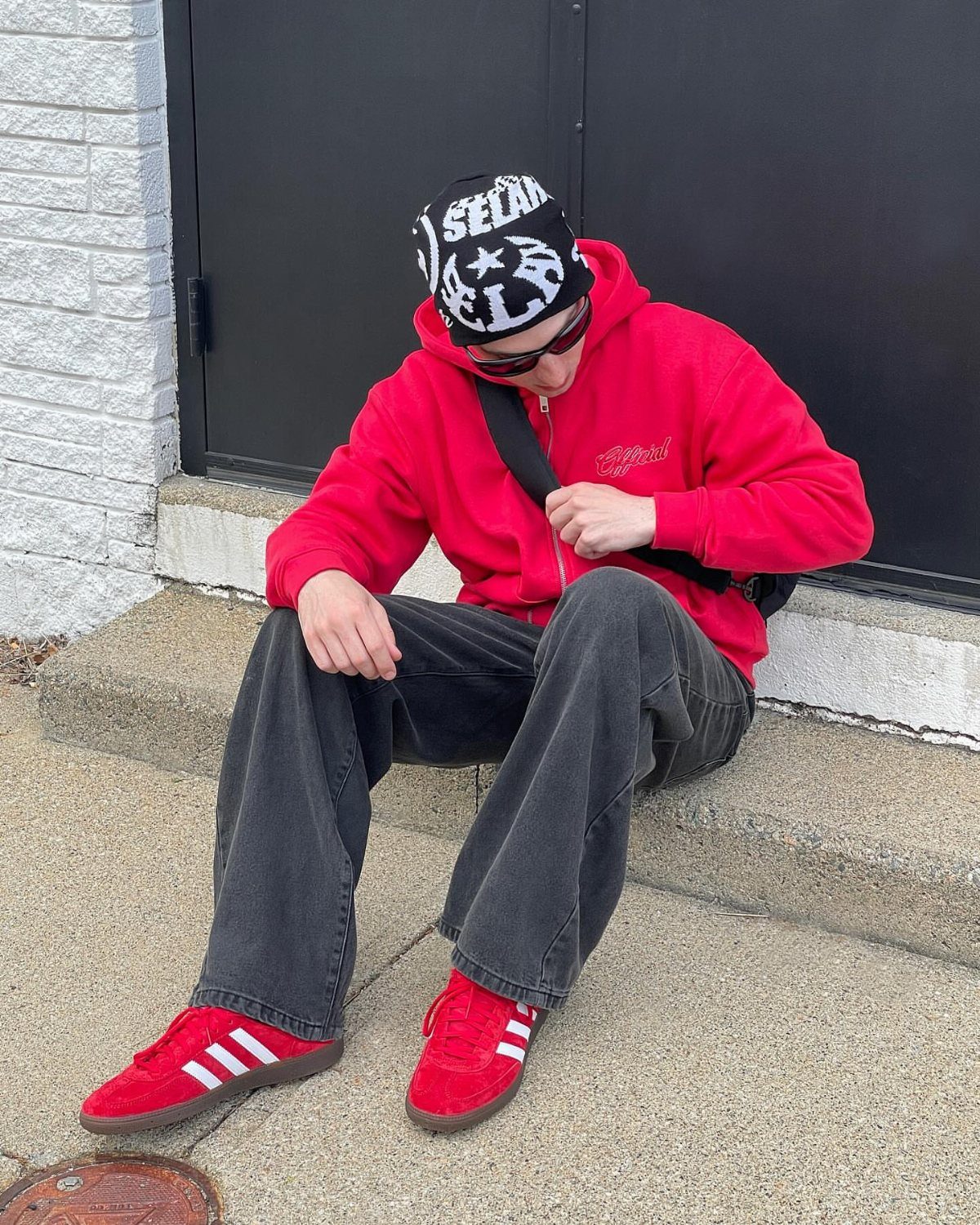 Person wearing red Adidas Samba sneakers, dark grey jeans, and a red hoodie.