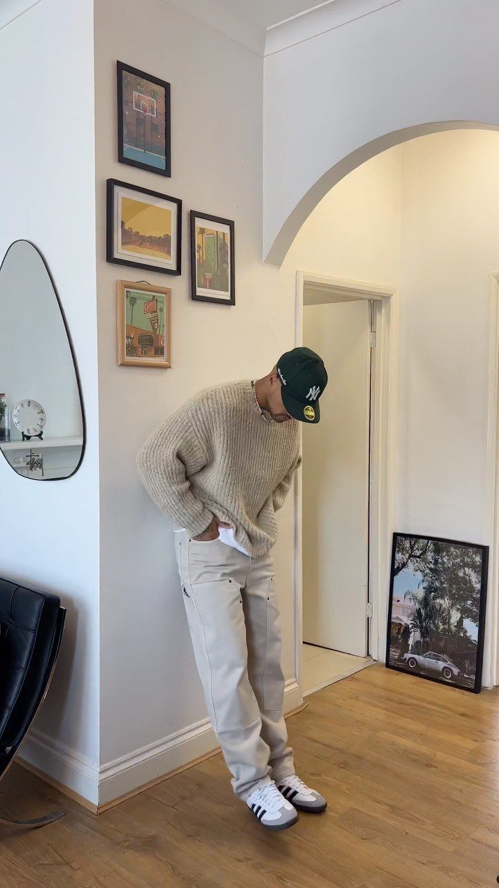 Person wearing a beige knit sweater, light trousers, and white Adidas Samba sneakers.