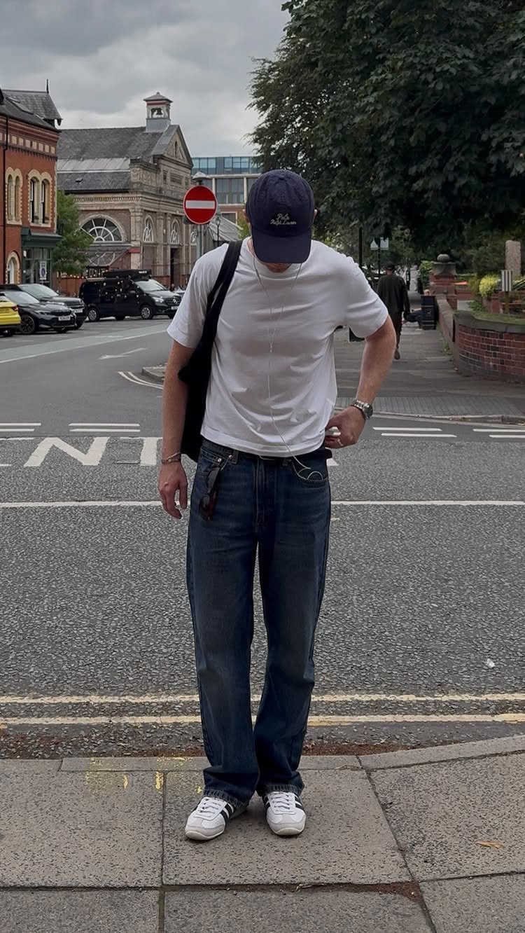 Person wearing a white t-shirt, blue jeans, and white Adidas Samba sneakers.