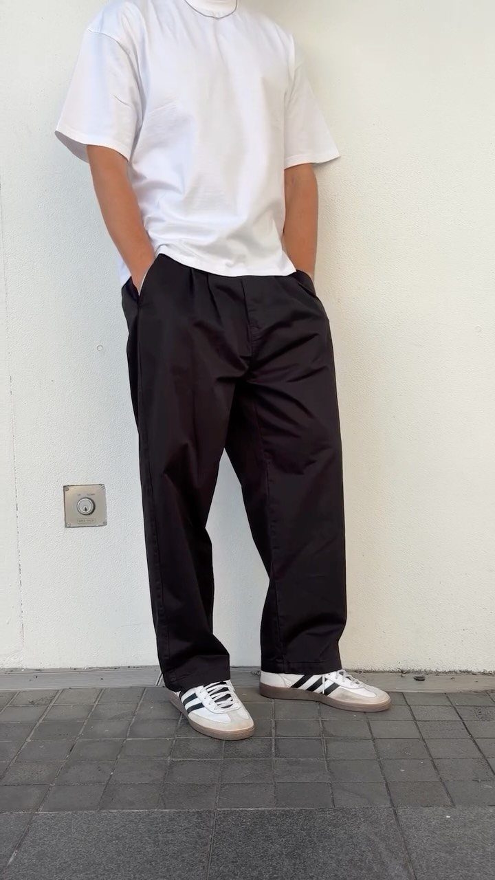 Person wearing a white t-shirt, black wide leg trousers, and white Adidas Samba sneakers.