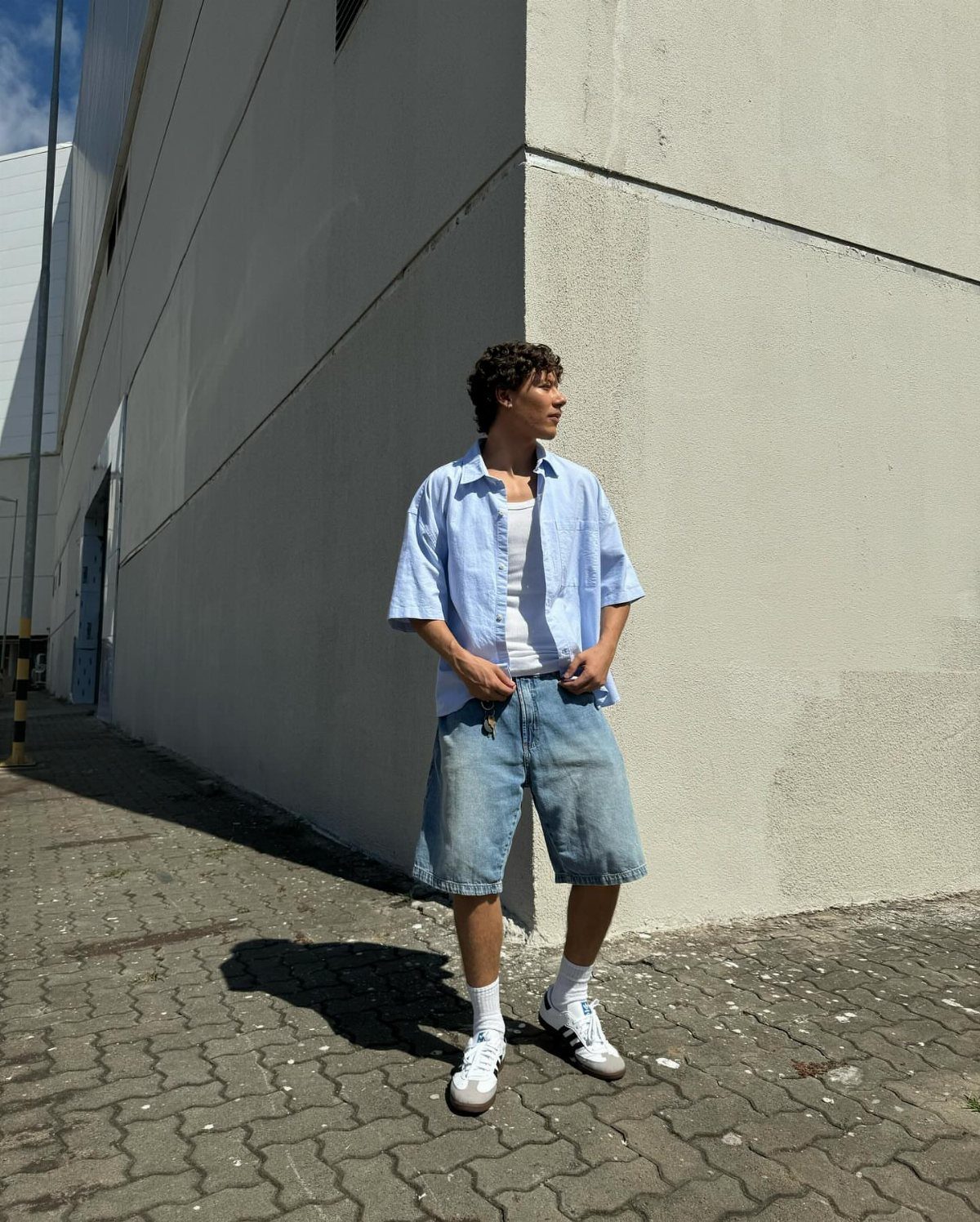 Man wearing a light blue button-down shirt and baggy denim shorts outdoors.
