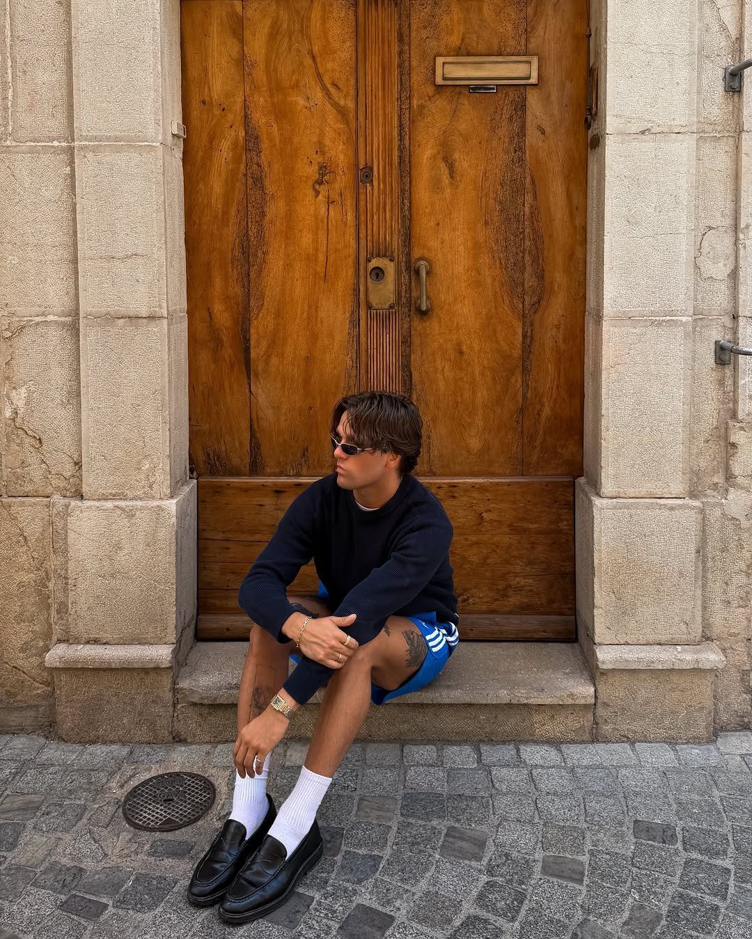 Man wearing navy shirt and blue Adidas shorts sitting by a wooden door
