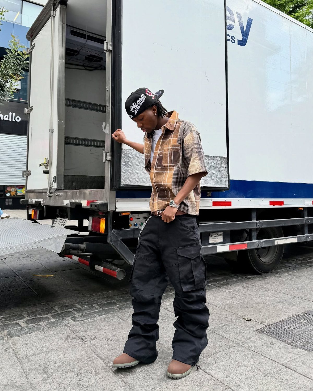 Man wearing a plaid shirt, baggy black cargo pants, and tan boots.