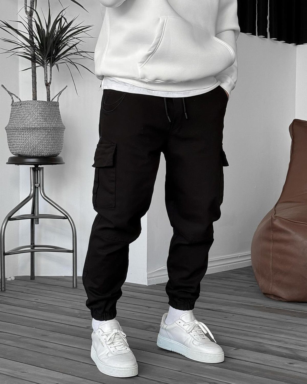 Person wearing black cargo pants, white oversized hoodie, and white sneakers indoors.