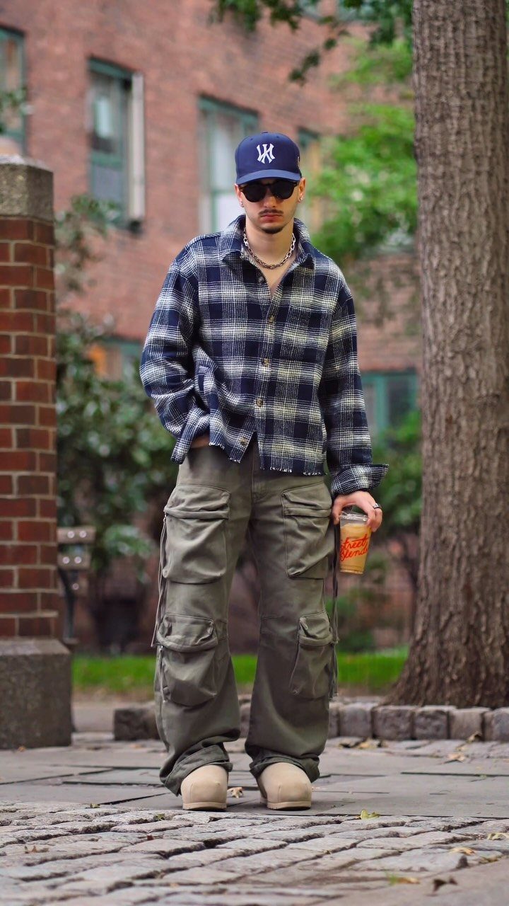 Man in olive green baggy cargo pants, plaid shirt, and blue baseball cap.