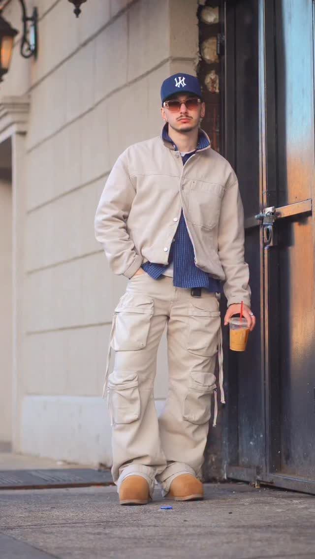 Man wearing beige cargo pants, a beige jacket, and a blue baseball cap.