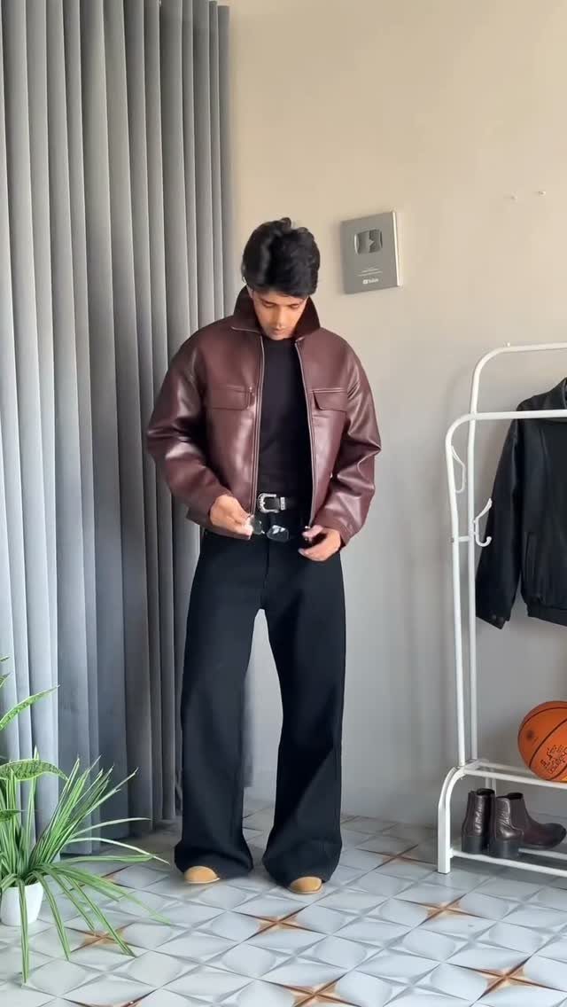 Man wearing a brown leather jacket and wide-leg black baggy jeans indoors.