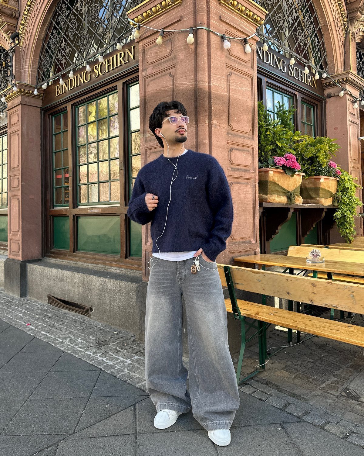Man wearing a navy fuzzy sweater and grey baggy jeans standing outdoors.