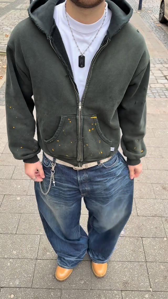 Man wearing an oversized green hoodie and baggy blue jeans on a sidewalk