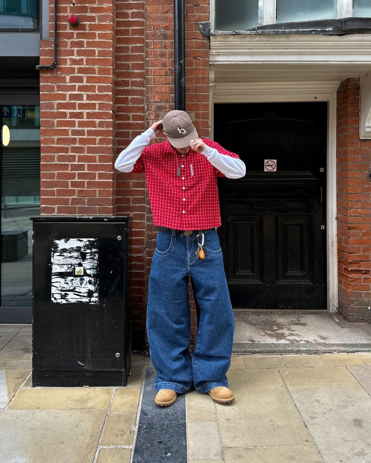 Man wearing a red checkered oversized shirt layered over white, with baggy blue jeans.