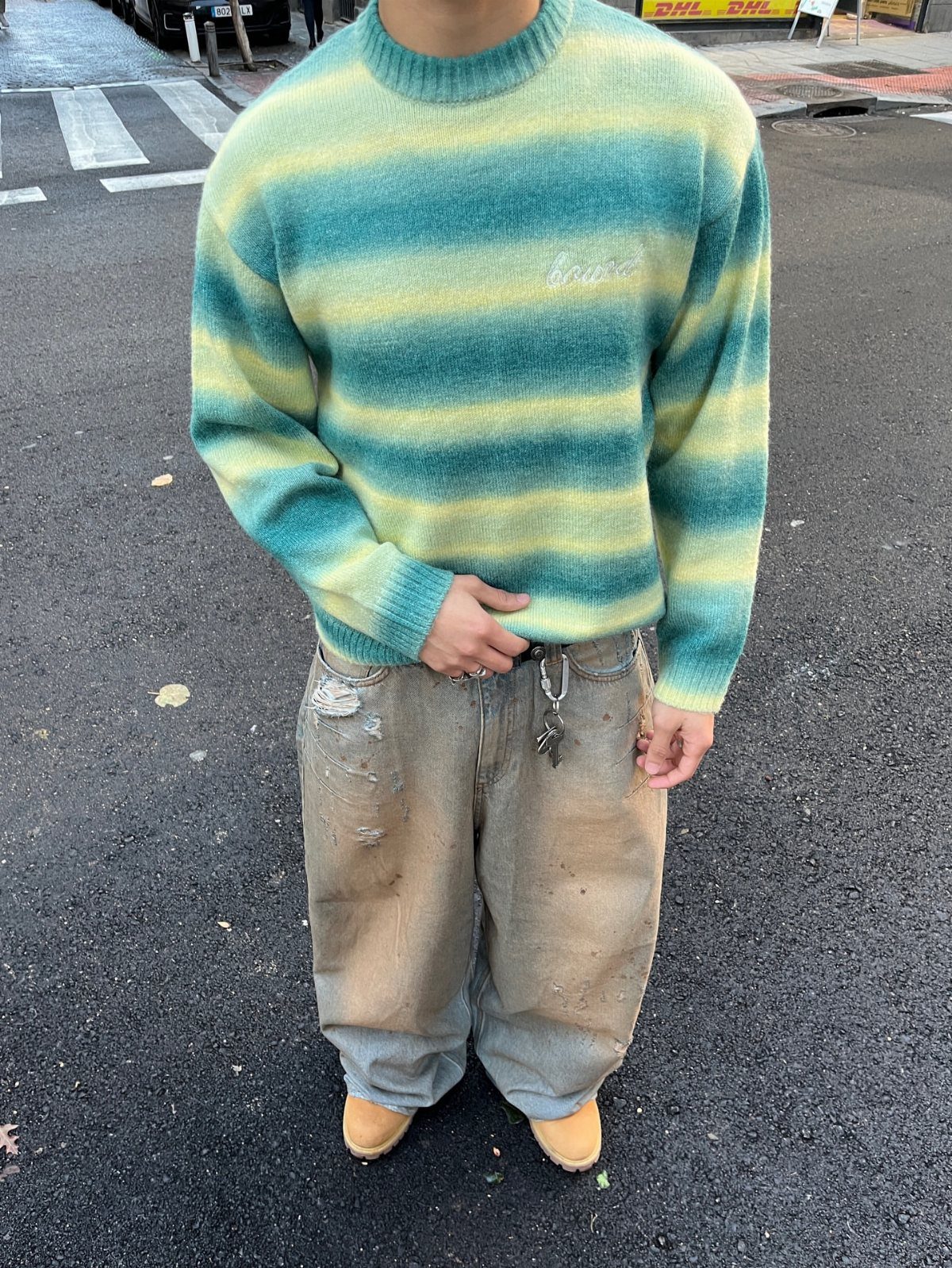 Person wearing a striped oversized sweater and baggy distressed light-wash jeans on street.