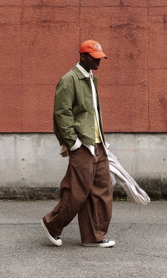 Man wearing an orange cap, olive jacket, and baggy brown trousers walking outdoors.