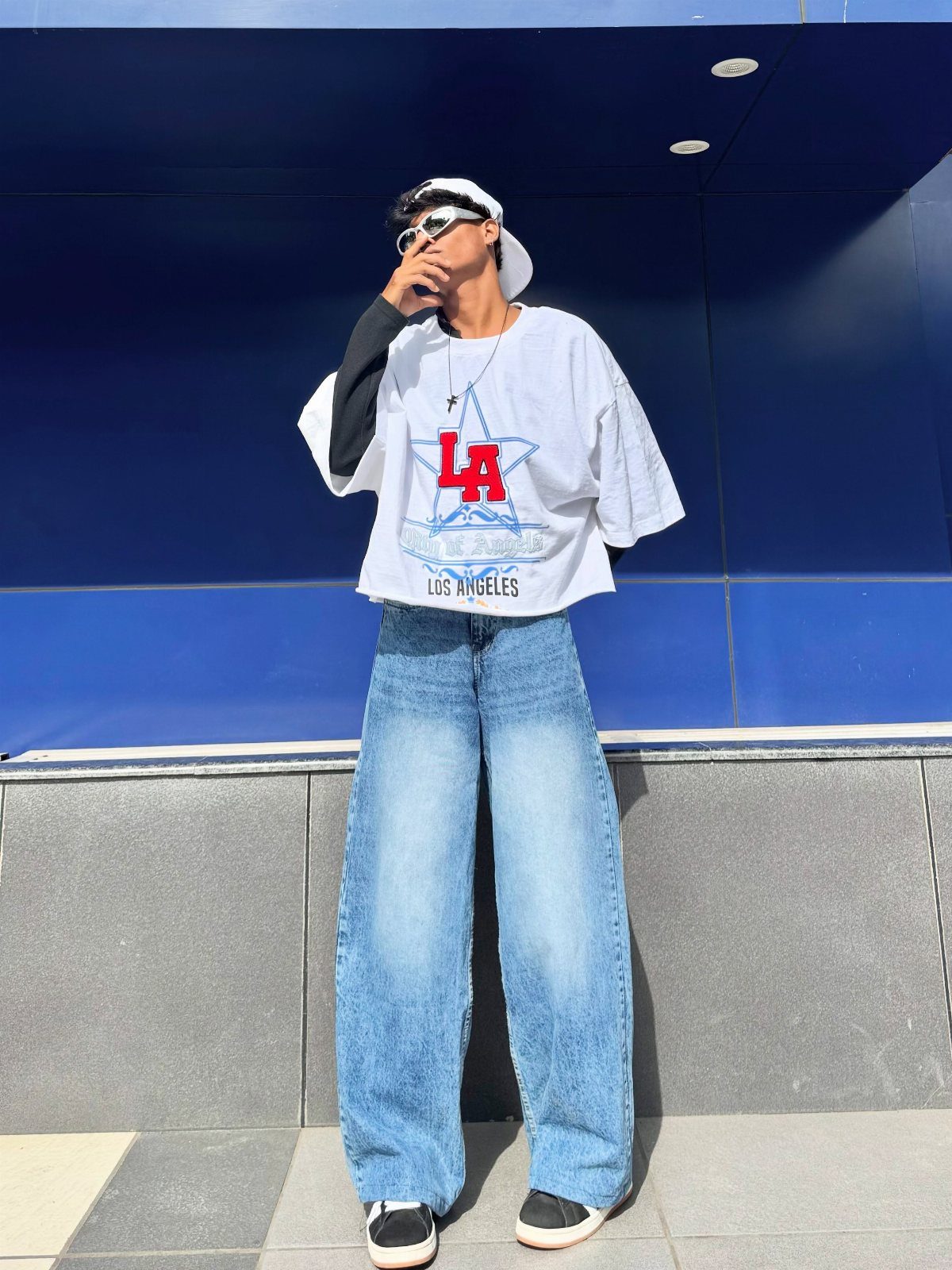 Man in white graphic t-shirt and wide-leg blue denim jeans posing outdoors.