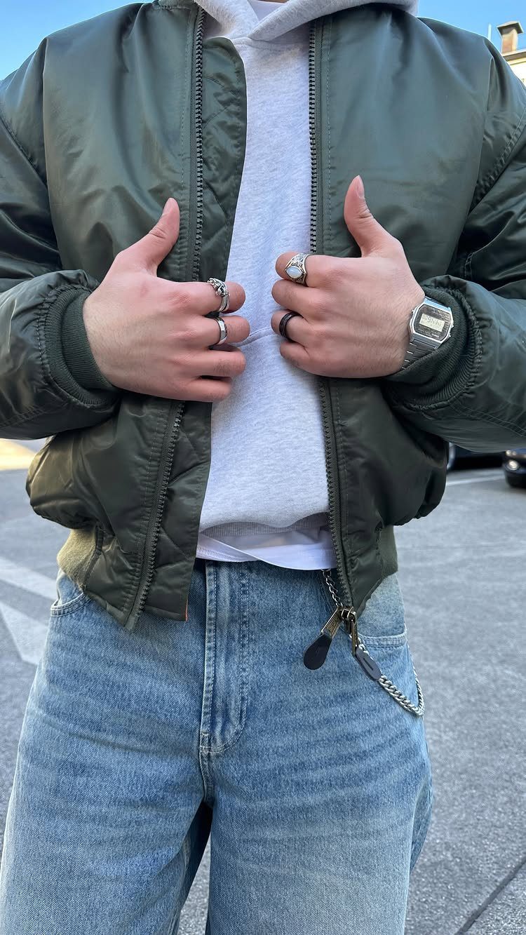 Man wearing an olive green bomber jacket over a grey hoodie and blue jeans.