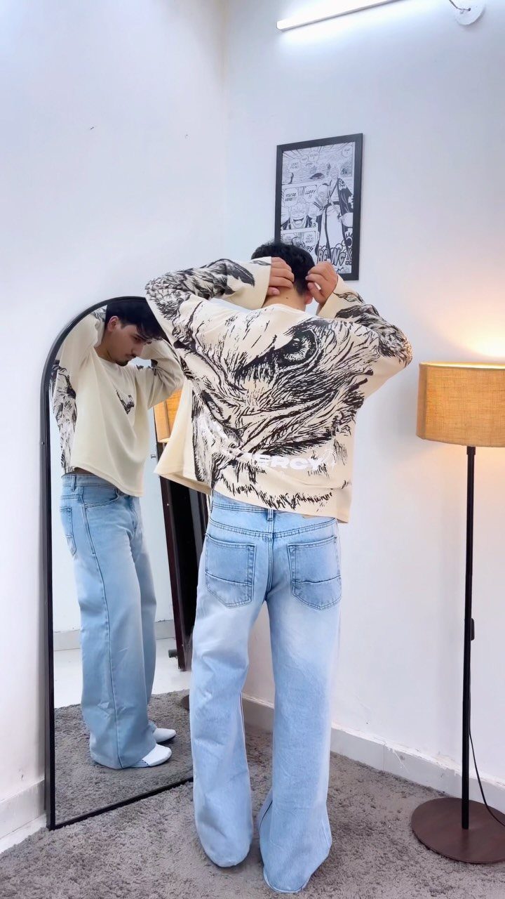 Man wearing an oversized graphic t-shirt and baggy light-wash jeans in a room.