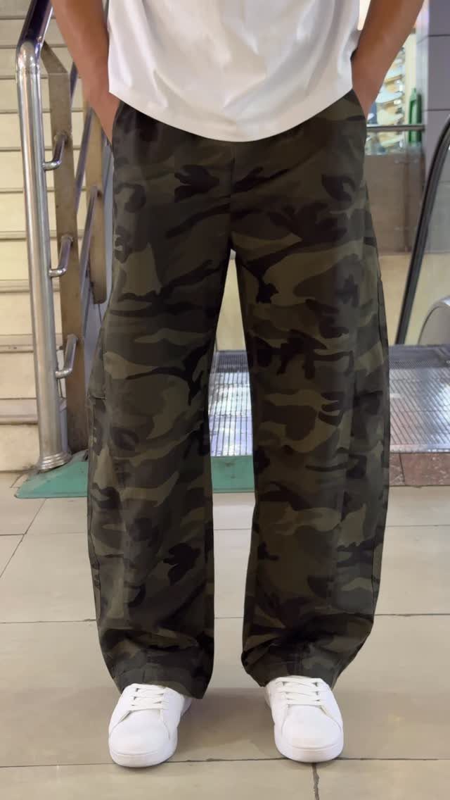 Person wearing wide-leg camouflage trousers, a white t-shirt, and white sneakers.