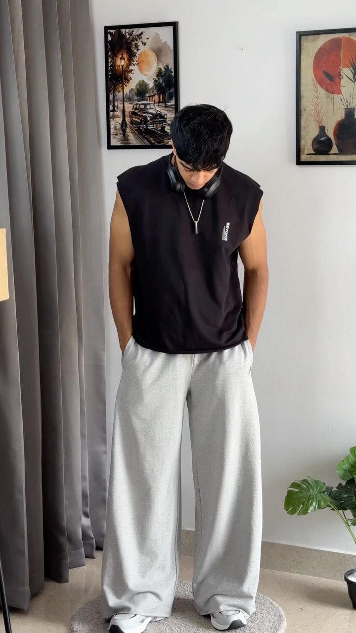Man in black sleeveless top and oversized grey sweatpants standing in a room.