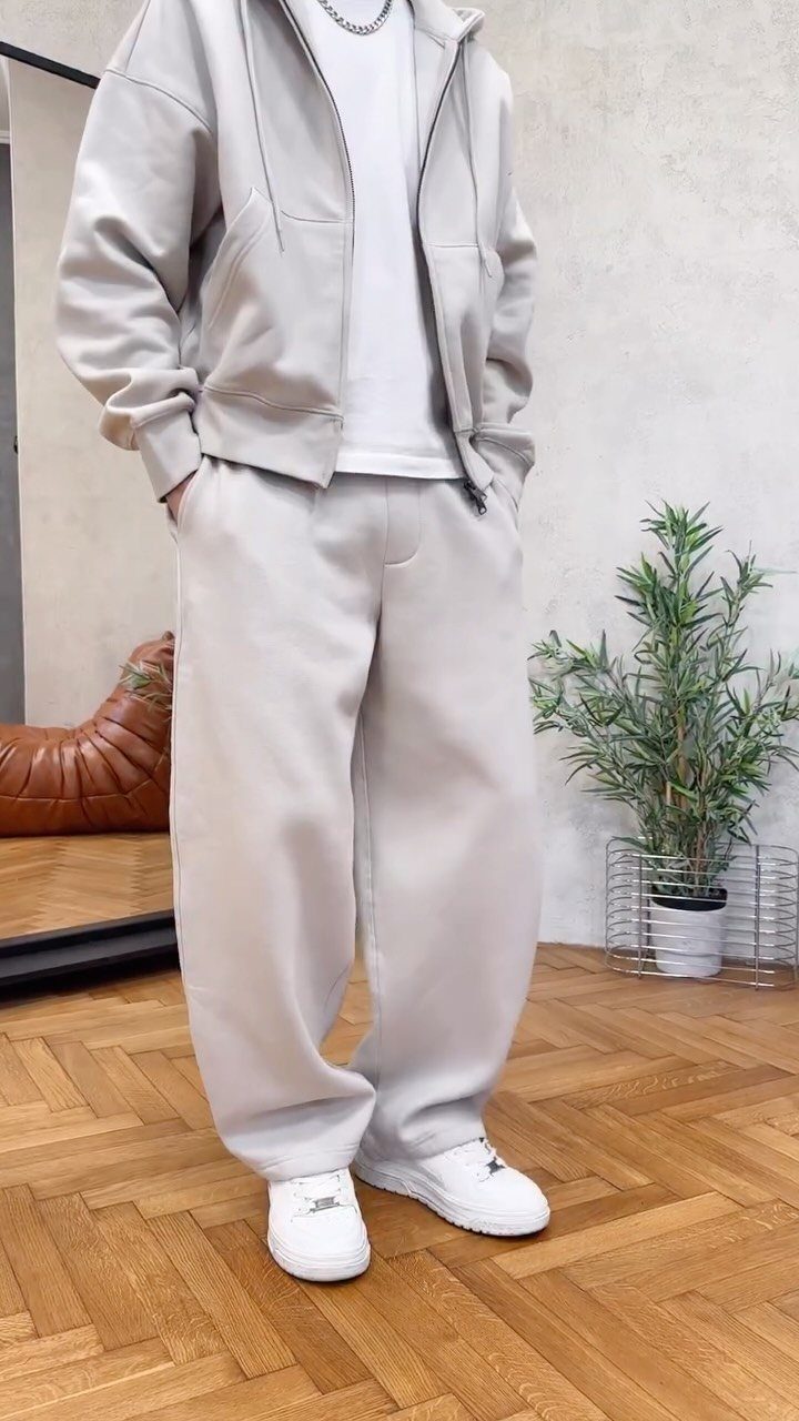 Person wearing a monochrome light grey oversized sweatsuit with white sneakers.