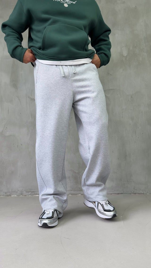 Person wearing a dark green hoodie and oversized light grey baggy sweatpants with sneakers.