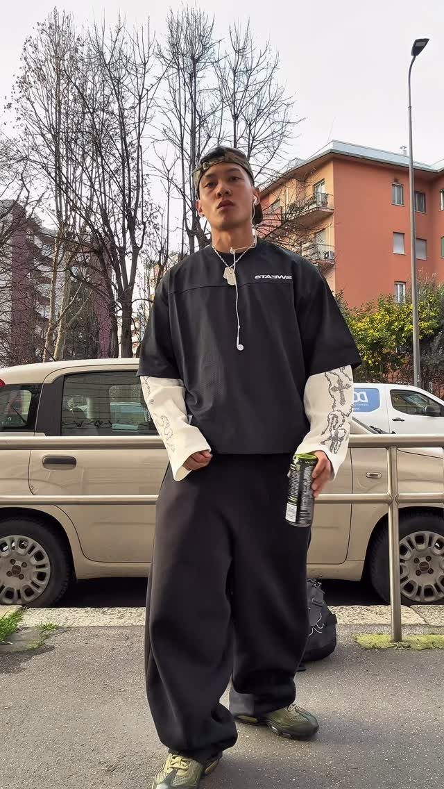 Person wearing a black oversized t-shirt and baggy black sweatpants standing outdoors.