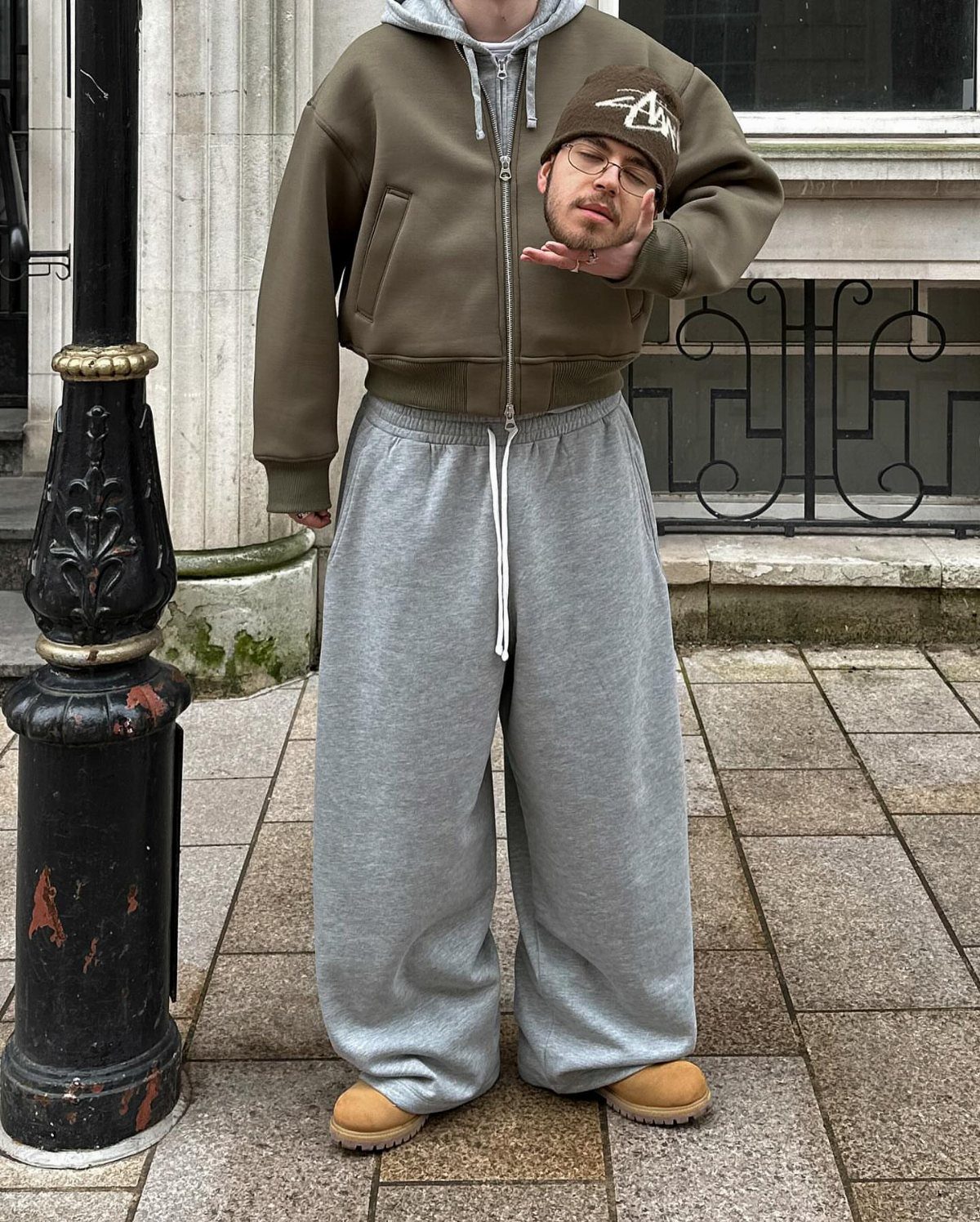 Person wearing olive bomber jacket and baggy grey sweatpants on a city street.