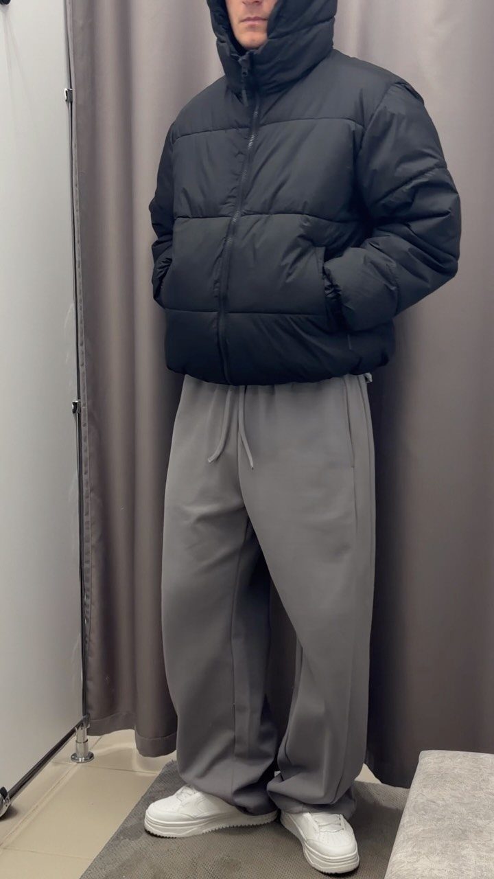 Person wearing a black puffer jacket and grey baggy sweatpants with white sneakers.