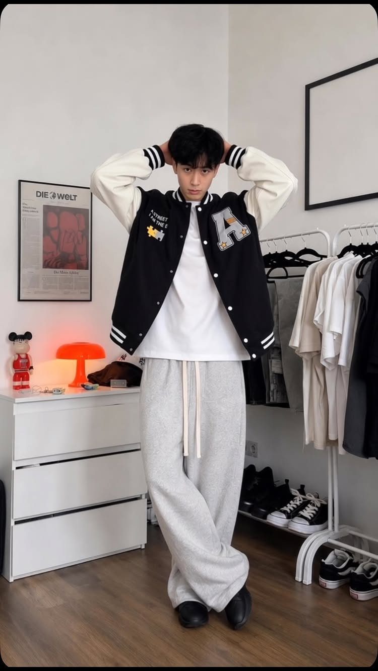 Man wearing a black and white varsity jacket with baggy grey sweatpants.