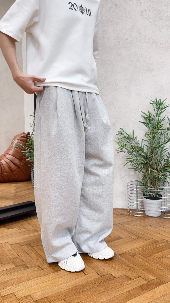 Person wearing oversized light grey sweatpants, a white t-shirt, and white sneakers.