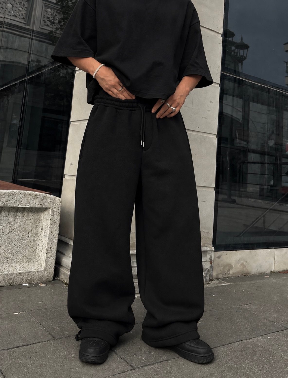 Person wearing baggy black sweatpants, a black t-shirt, and black sneakers outdoors.