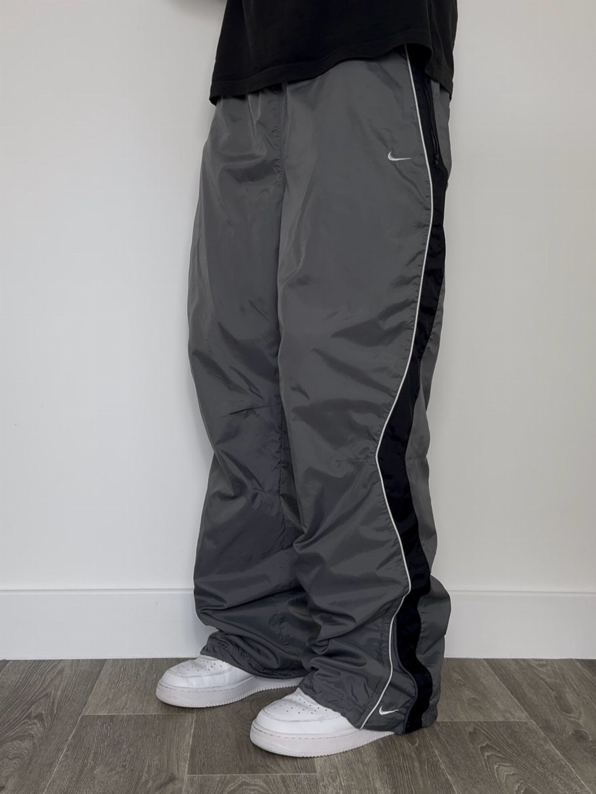 Baggy grey nylon sweatpants with black side stripes and white leather sneakers.