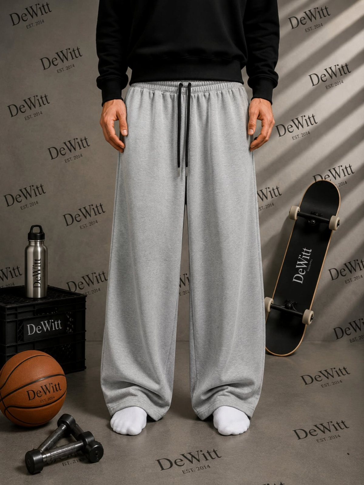 Person wearing wide-leg grey sweatpants and black sweatshirt with sports equipment around them