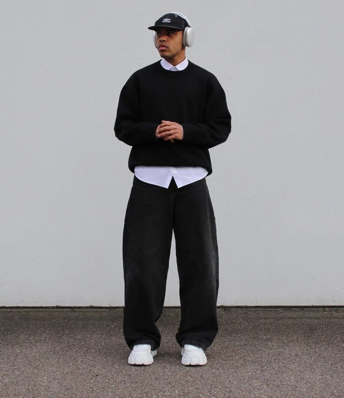 Man in black crewneck sweater and baggy black trousers with white sneakers