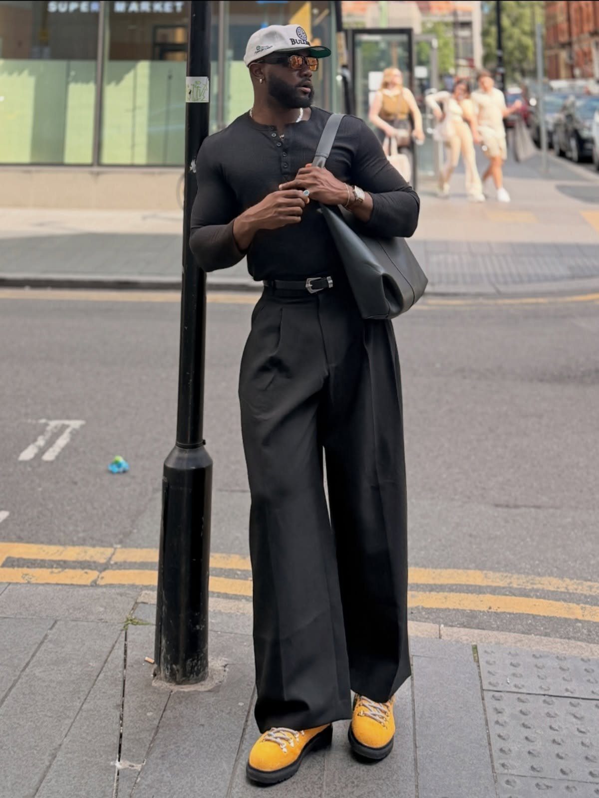 Man in black long-sleeve shirt and wide-leg trousers wearing bright yellow shoes.