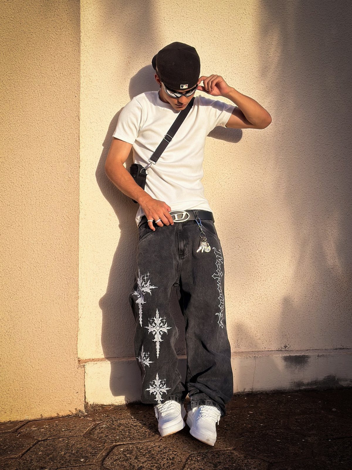 Person in white t-shirt and baggy black jeans with white patterns and sneakers.