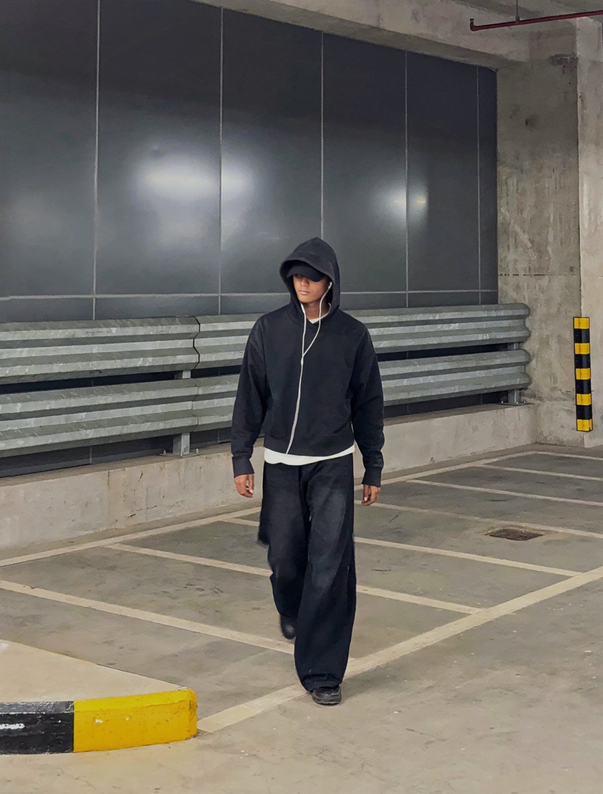 Person wearing a black oversized hoodie and baggy black sweatpants in a parking garage.