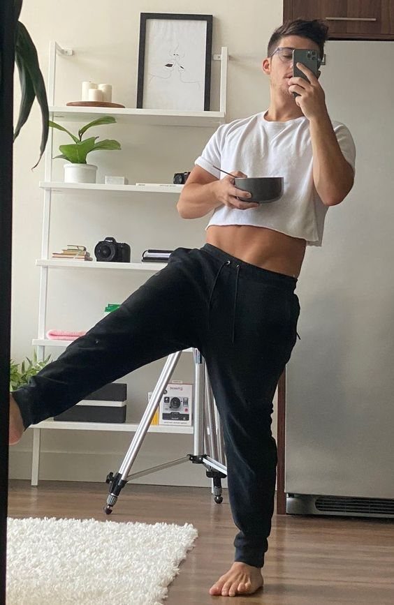 Man in white cropped t-shirt and baggy black sweatpants holding a bowl.