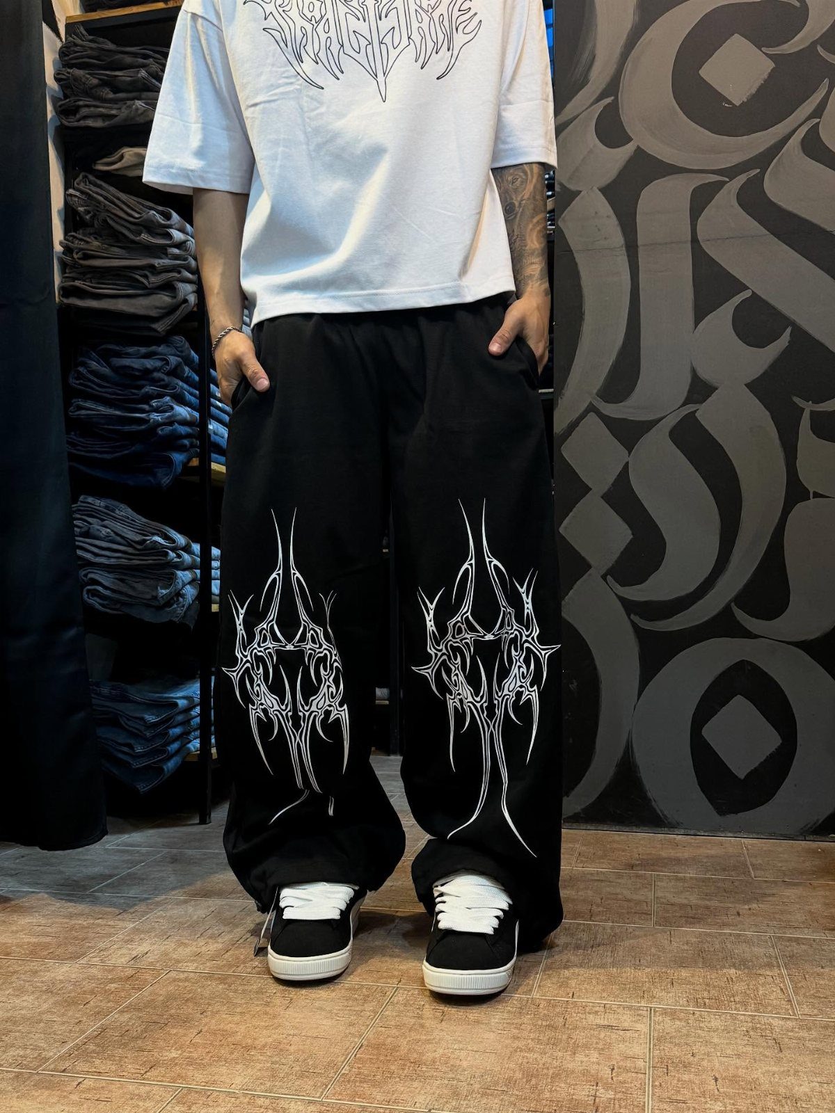 Person wearing a white graphic t-shirt and baggy black graphic sweatpants with sneakers.