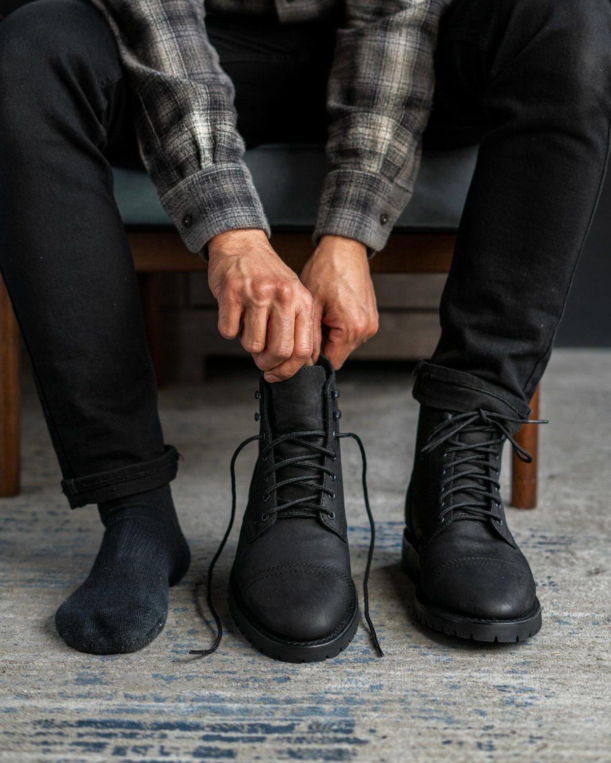 Person in plaid flannel shirt and black jeans tying black combat boots.