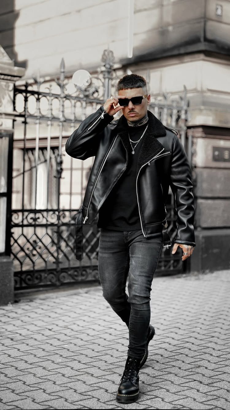 Man in black leather jacket, black jeans, and black boots standing by iron gate
