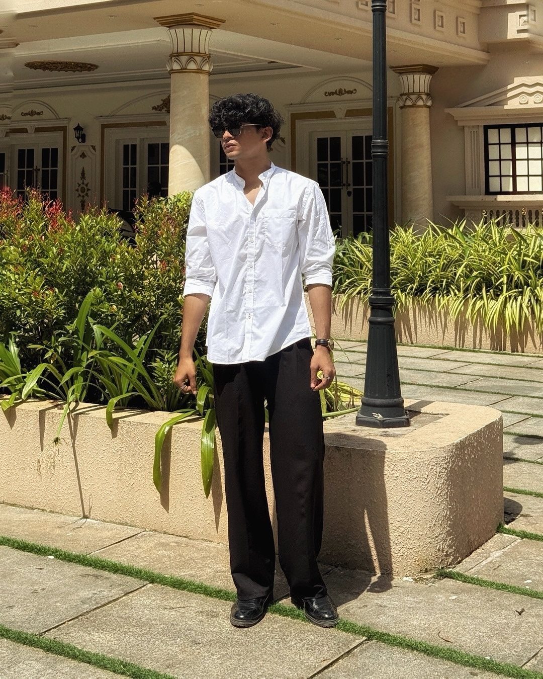 Man wearing a white button-down shirt, black wide-leg trousers, and black boots outdoors.