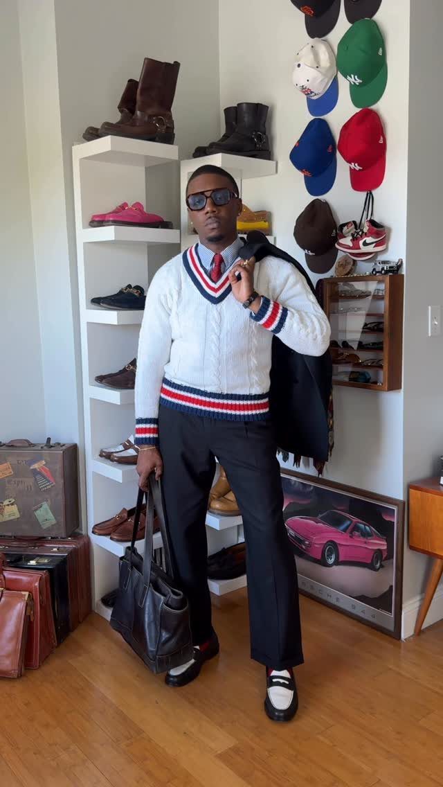 Man wearing black loafers, black trousers, and a white cable-knit sweater in a room.