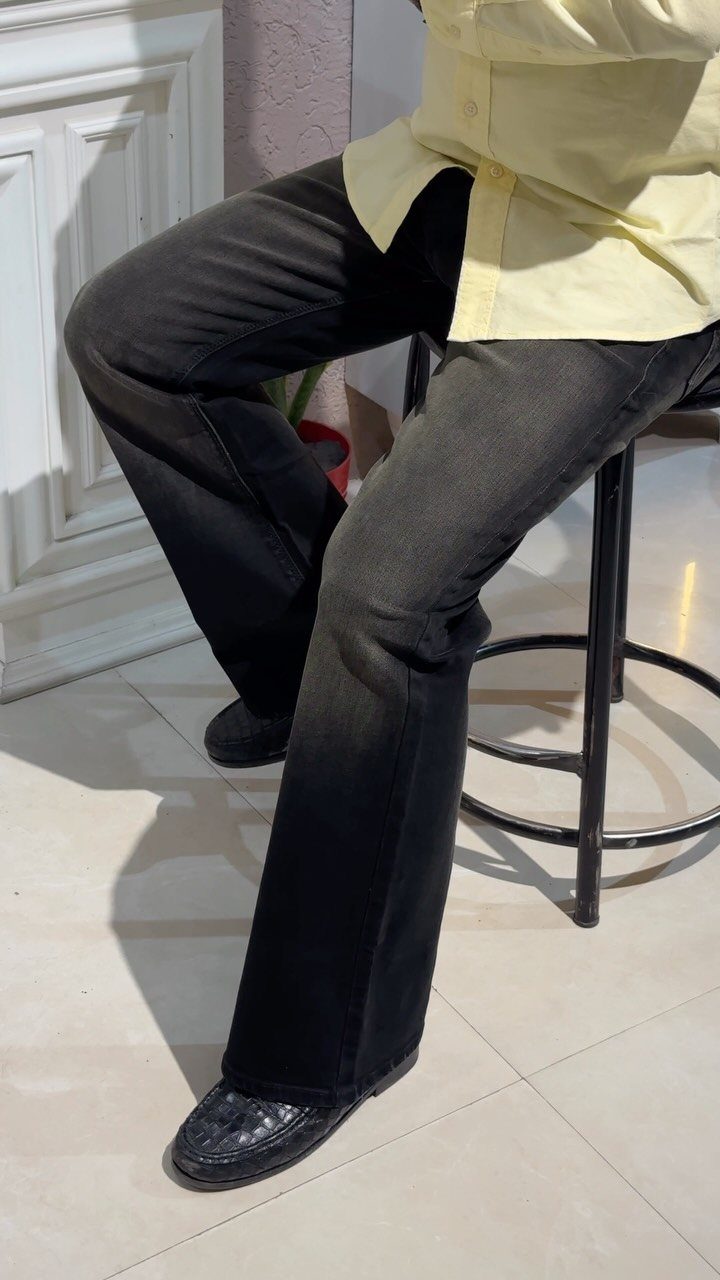 Person wearing black leather loafers with dark denim jeans and a yellow shirt.