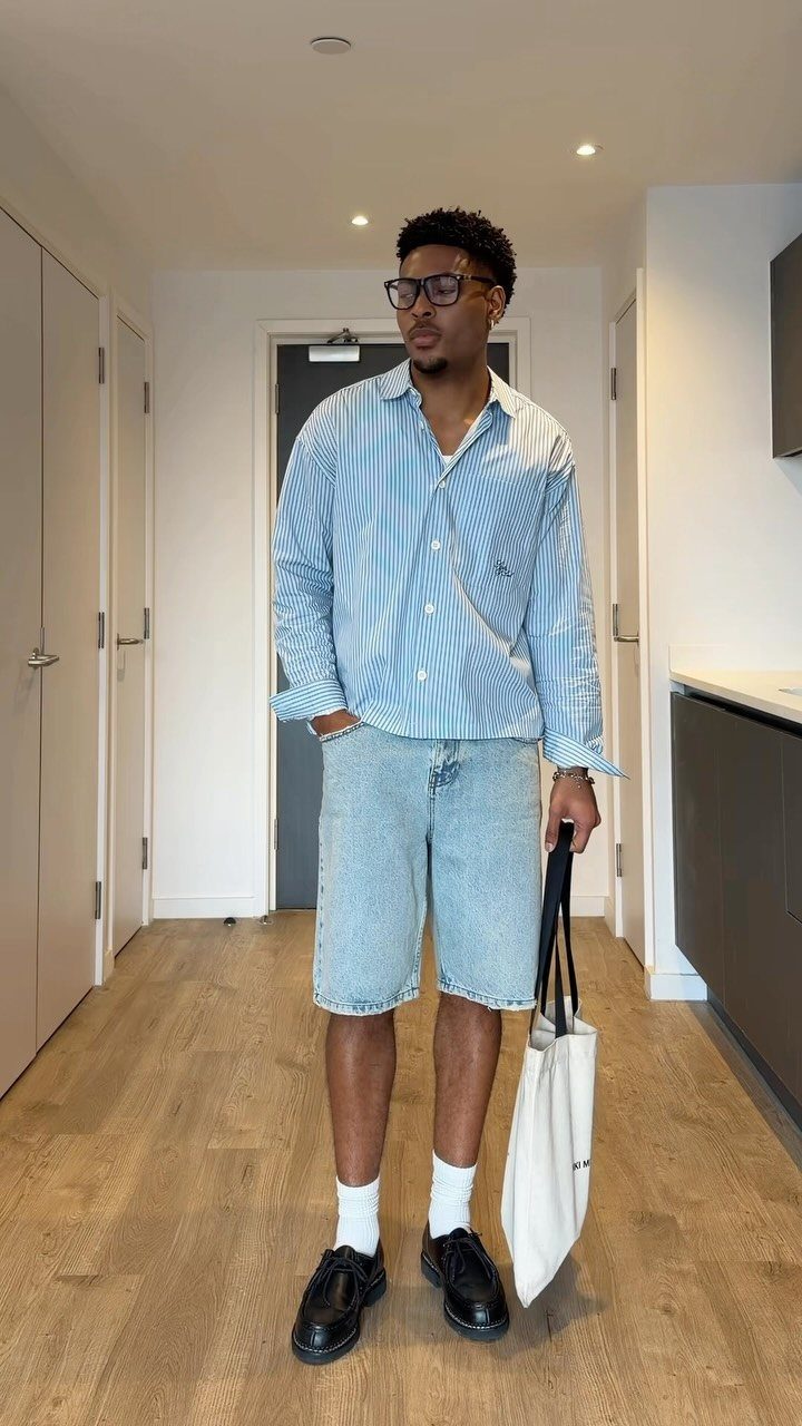 Man in striped shirt and denim shorts wearing black loafers and white socks.