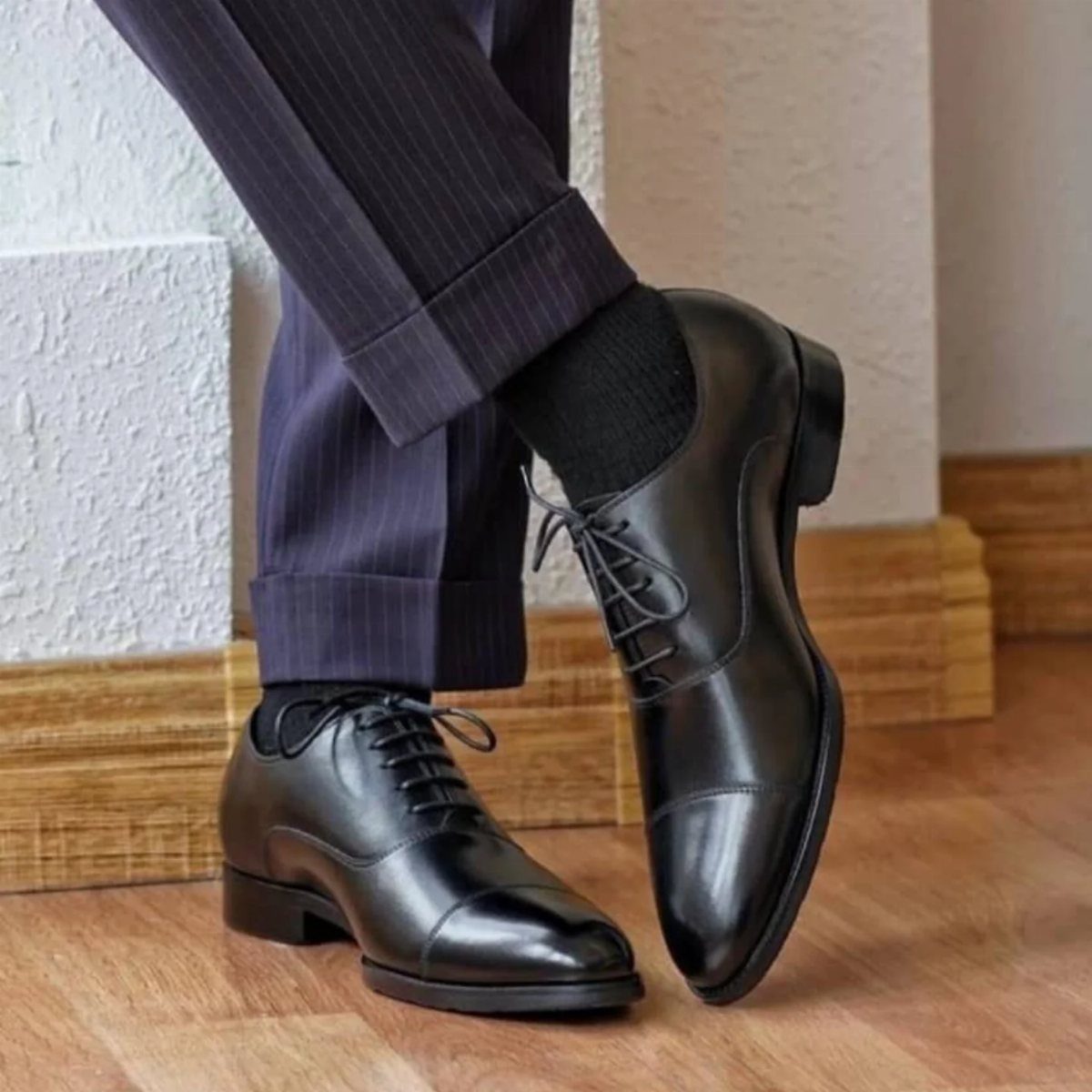 Black leather oxford shoes paired with dark grey pinstriped trousers and black socks.