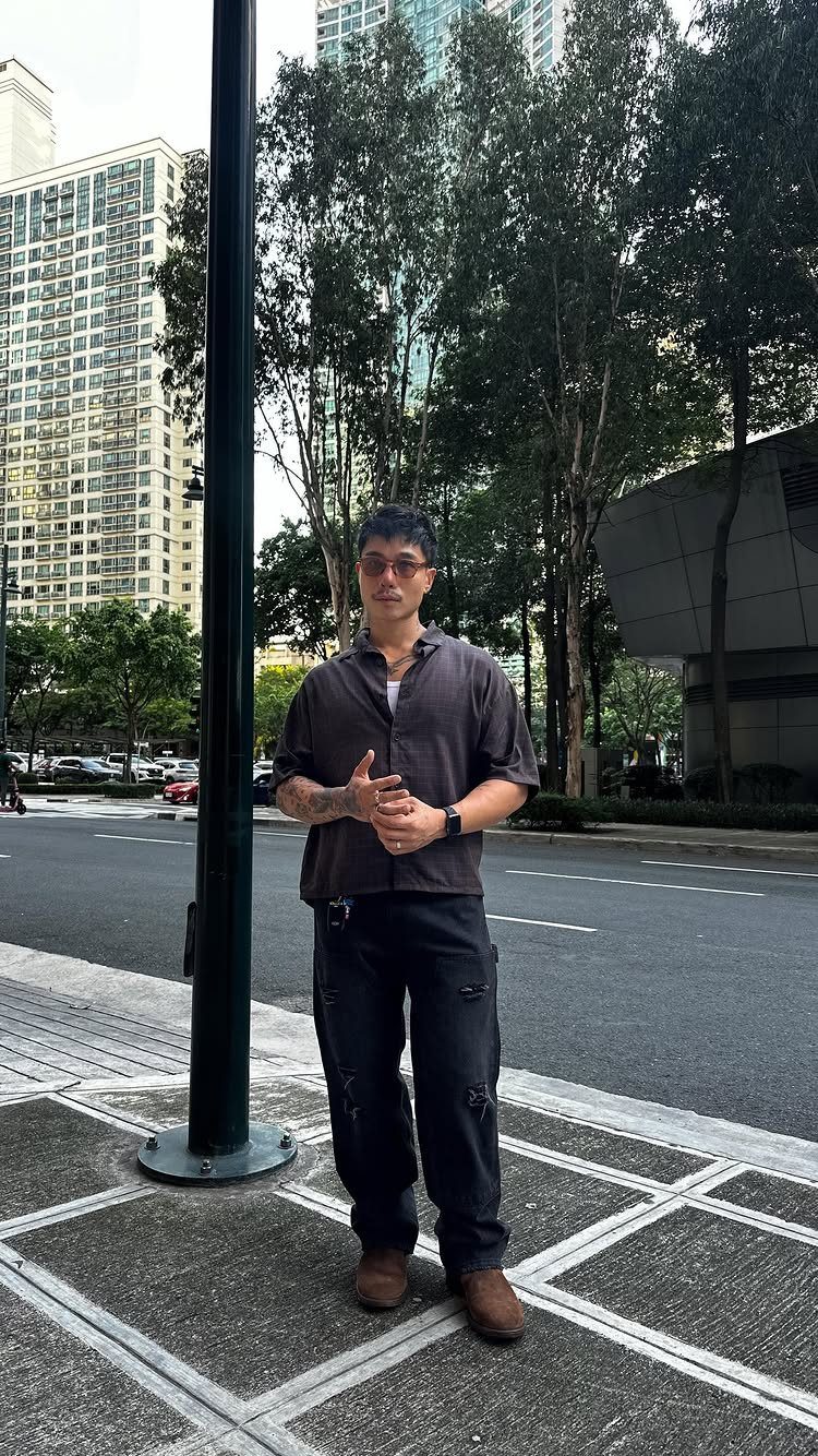Man in brown short-sleeved shirt, black cargo pants, and brown boots on city sidewalk.