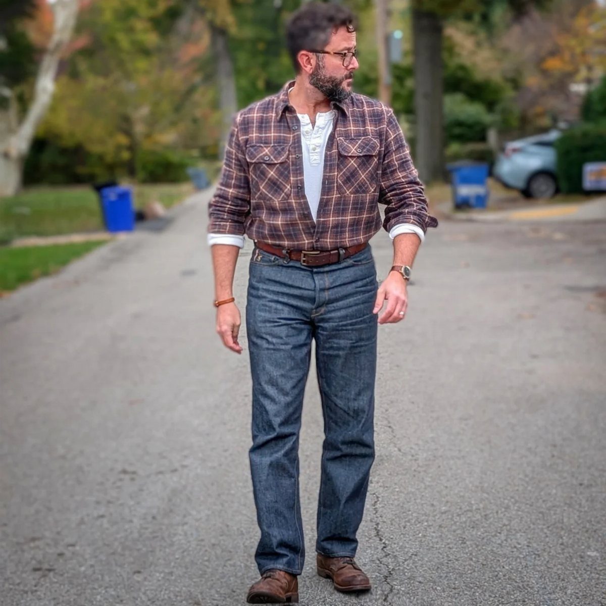 Man wearing brown leather boots, dark blue jeans, and a plaid button-down shirt.